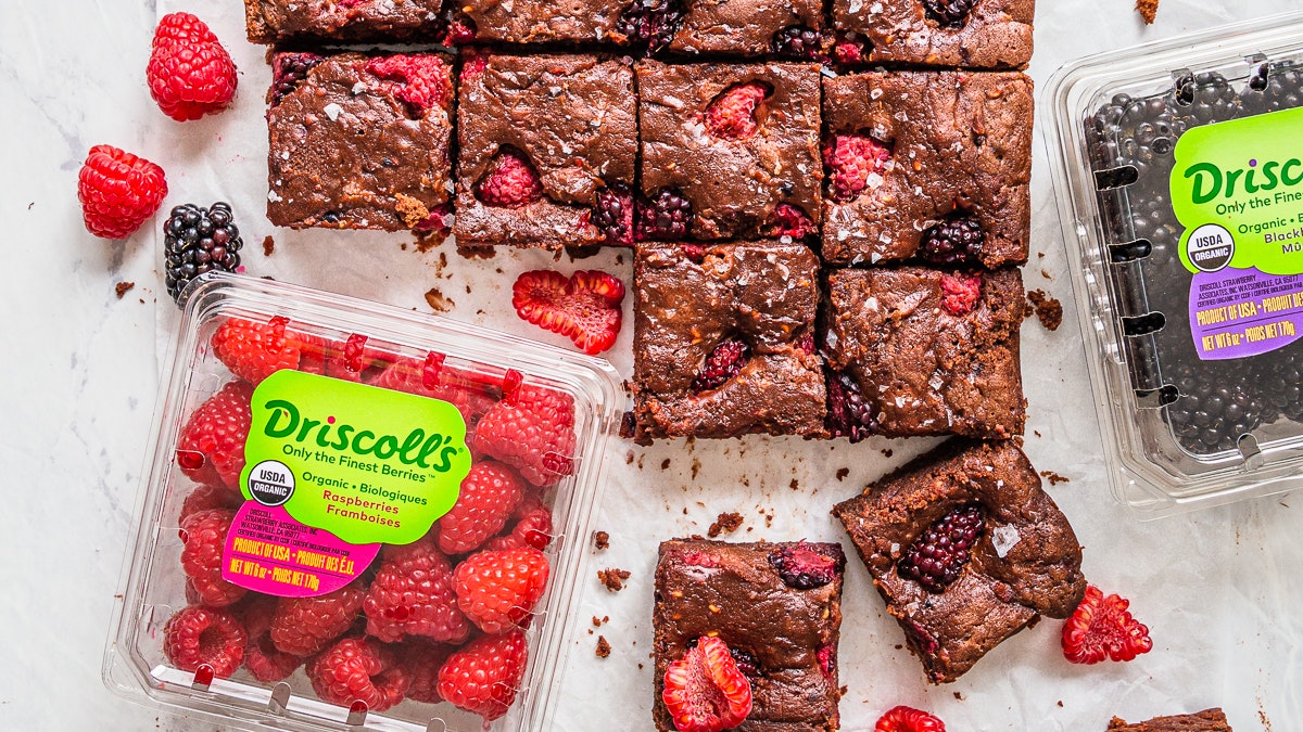 Squares of blackberry and raspberry brownies next to Driscoll's organic blackberry and raspberry clamshells.